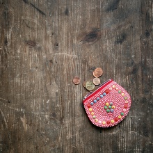 Ein roter Geldbeutel liegt auf einem Holztisch und drei Münzen vor ihm.